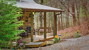 A rustic cabin with a wooden deck, seating area, and a covered porch.