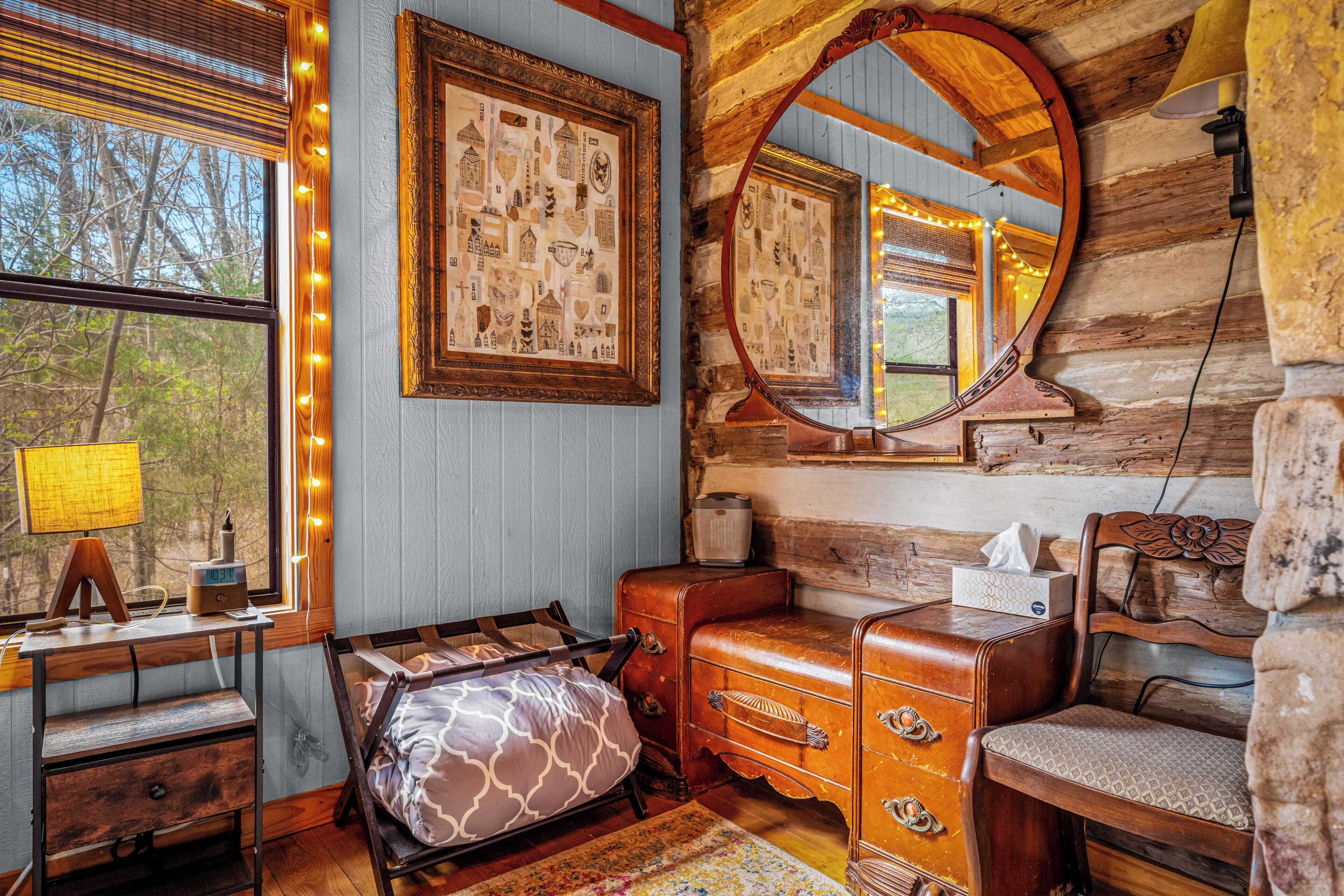 L’intérieur d’un chalet rustique, avec un bureau en bois, une commode, un miroir et une fenêtre décorée de guirlandes lumineuses.