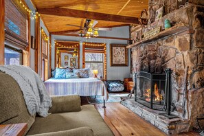 A cozy room with a stone fireplace, a bed with blue bedding, and a view of the outdoors through a window.