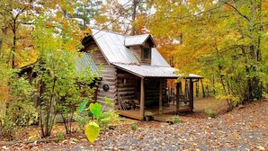 A rustic cabin with a porch, surrounded by autumn foliage.