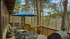A wooden deck with a table and chairs, a covered umbrella, and a grill.
