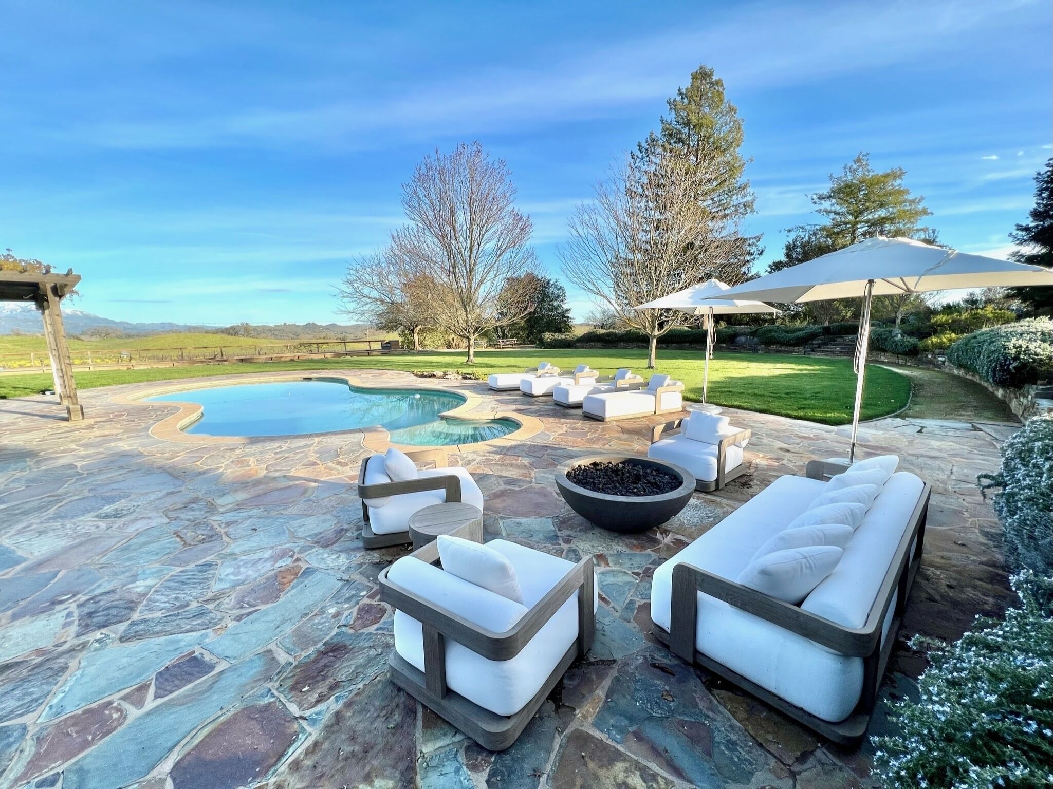 A stone patio with outdoor seating, a swimming pool, and a view of the surrounding landscape.
