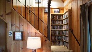 Una scala in legno conduce a una stanza piena di libri, con una lampada e quadri appesi alle pareti.