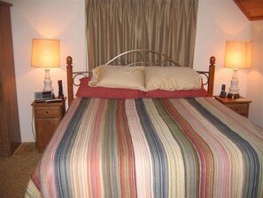 A bed with a striped bedspread, two bedside tables with lamps, and a curtain in the background. - Secluded, Romantic Getaway. Perfect for Families Too! (Pine Mountain Club)