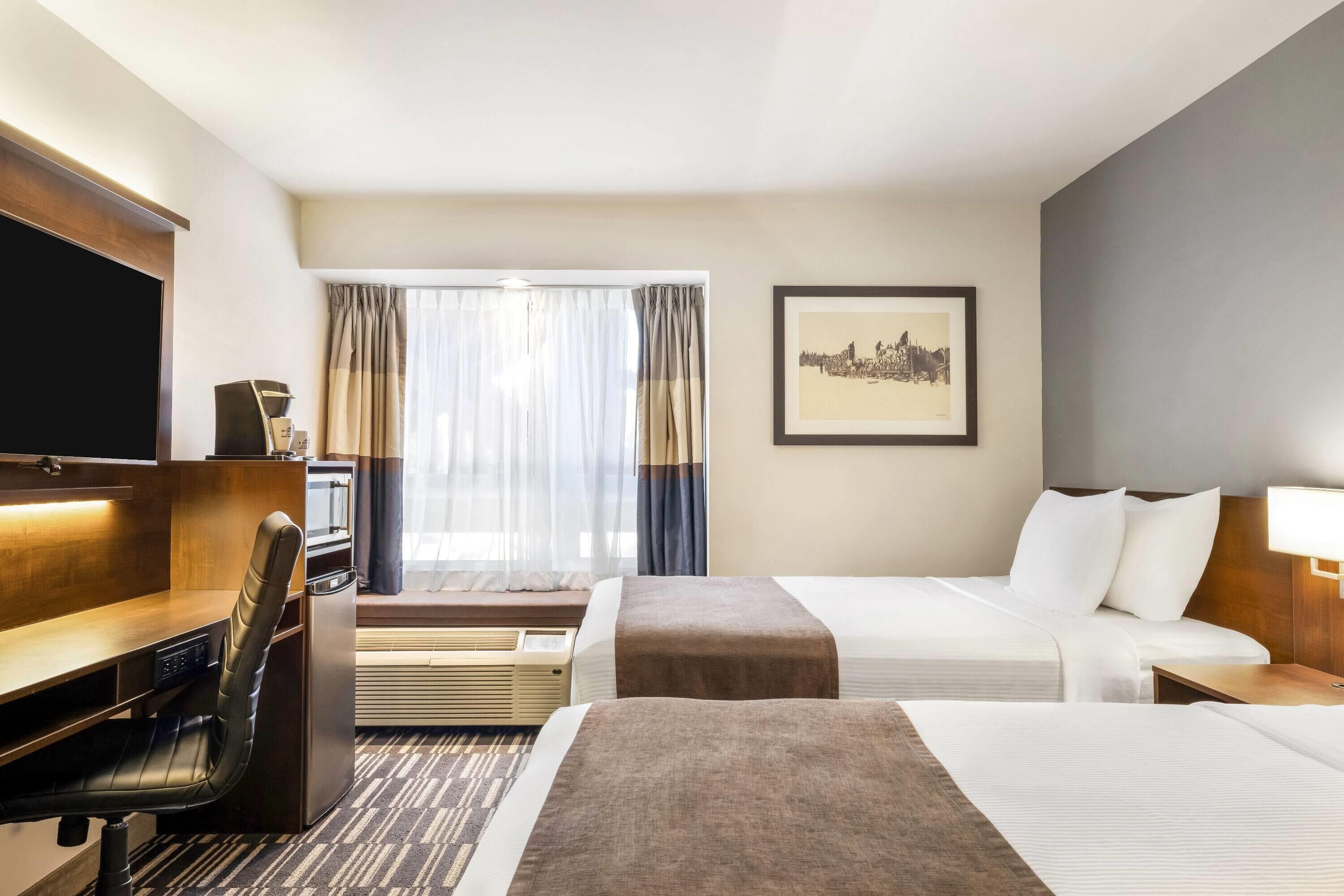 A hotel room with a desk, two beds, a TV, a framed picture, and a window with curtains.