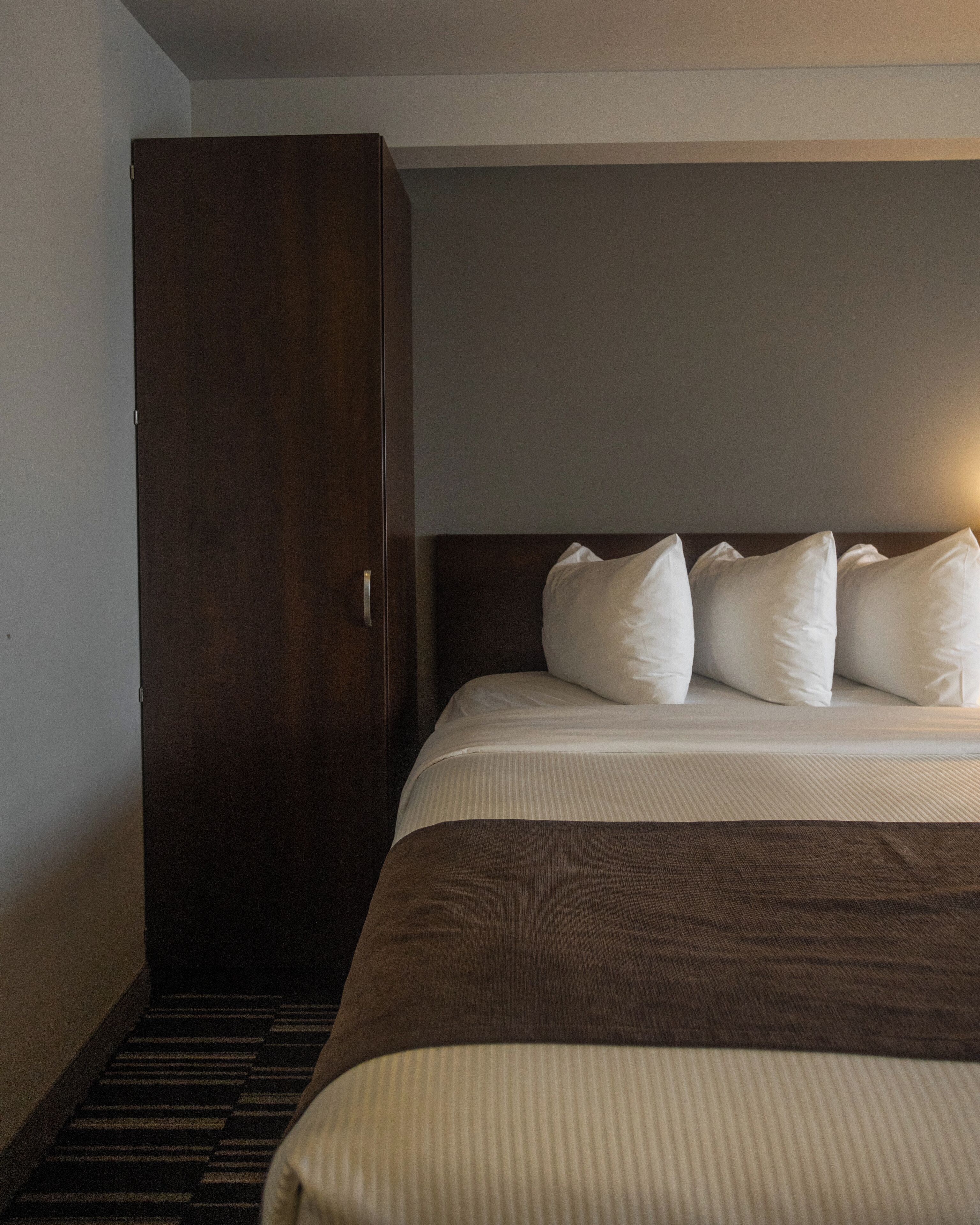 A hotel room with a large bed, a wardrobe, and a carpeted floor.