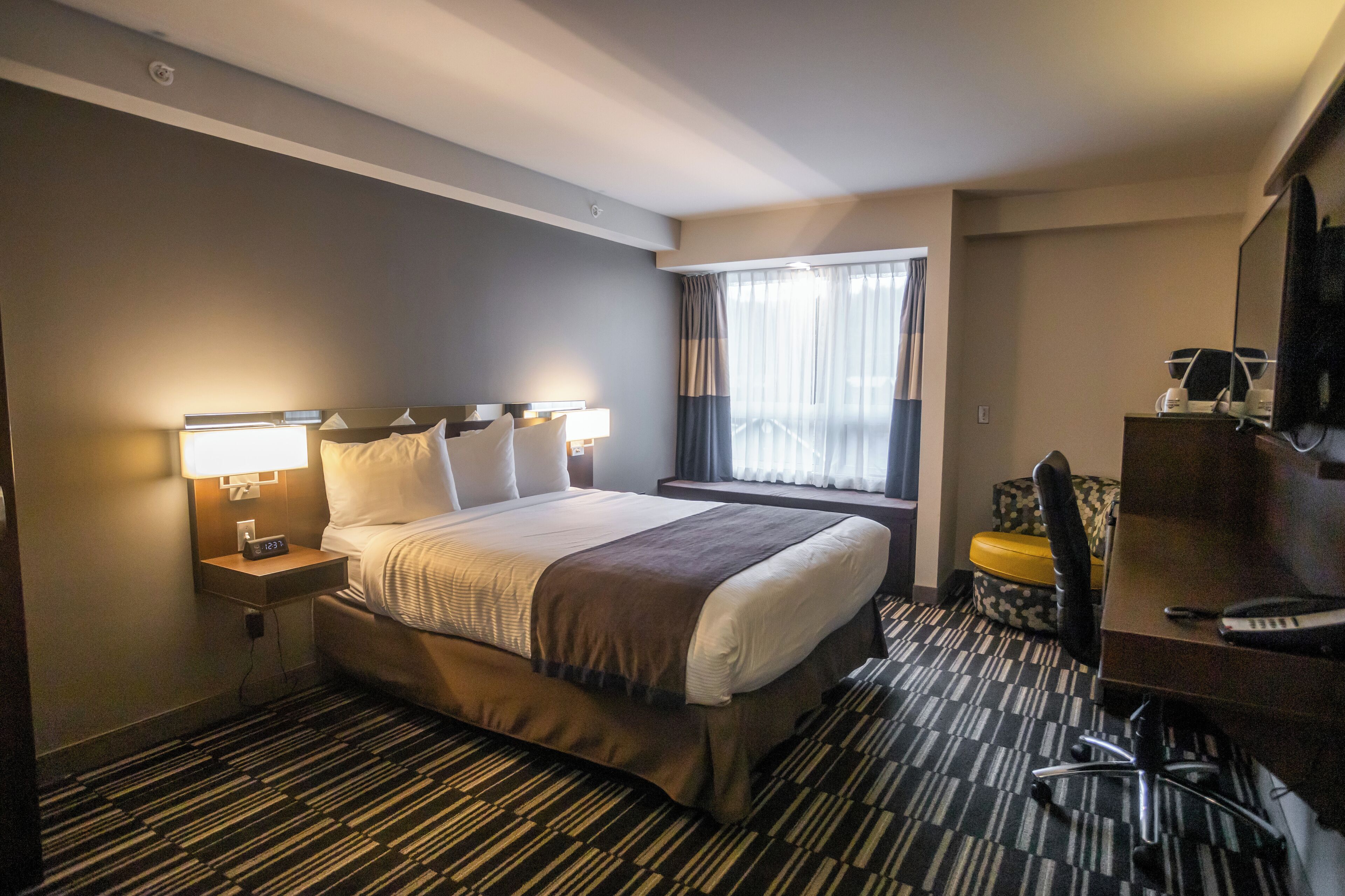 A hotel room with a large bed, a desk with a chair, a TV, and a window with curtains.