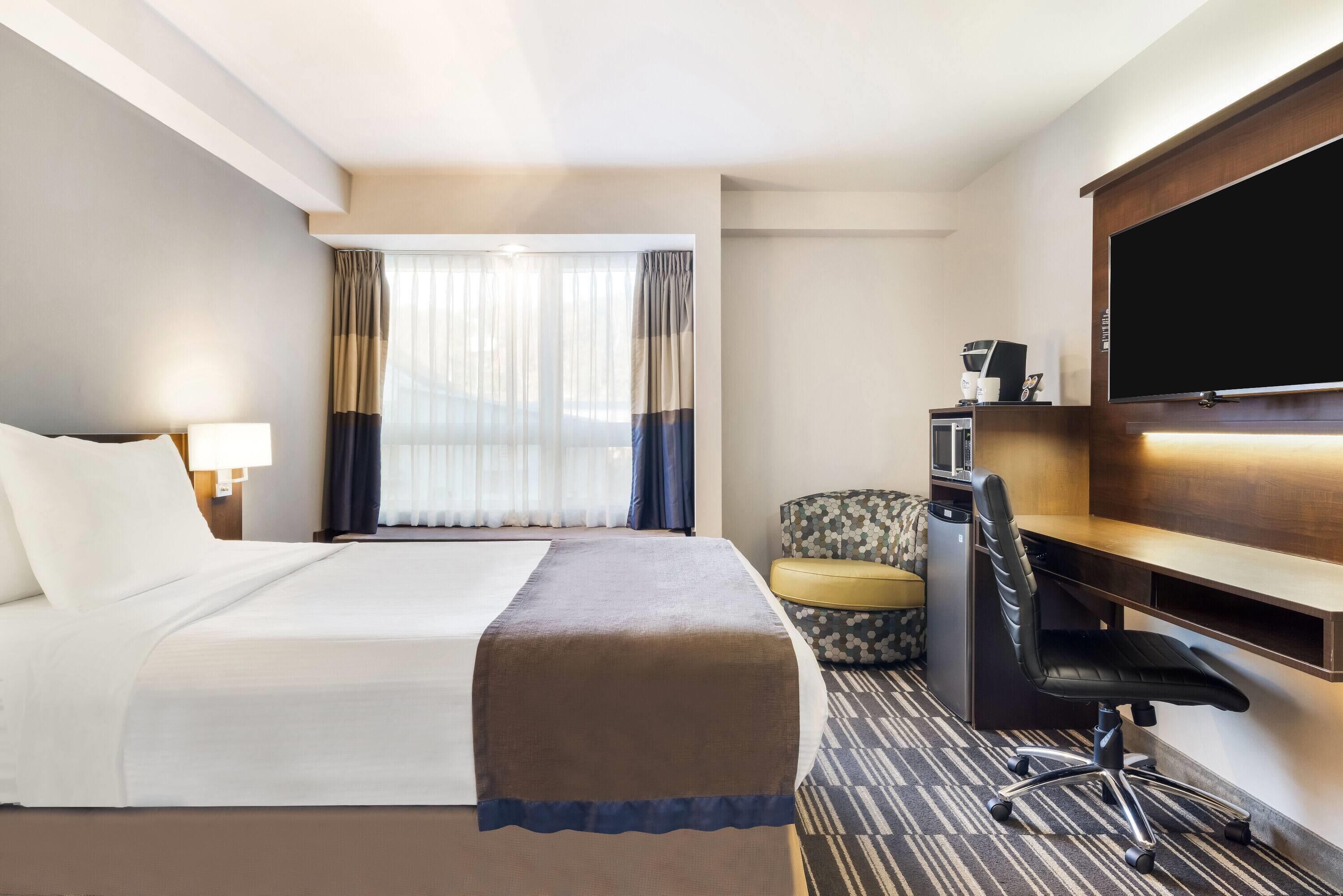 Ein Hotelzimmer mit Bett, Schreibtisch, Stuhl, Fernseher und einem Fenster mit Vorhängen.