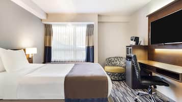 Ein Hotelzimmer mit Bett, Schreibtisch, Stuhl, Fernseher und einem Fenster mit Vorhängen.