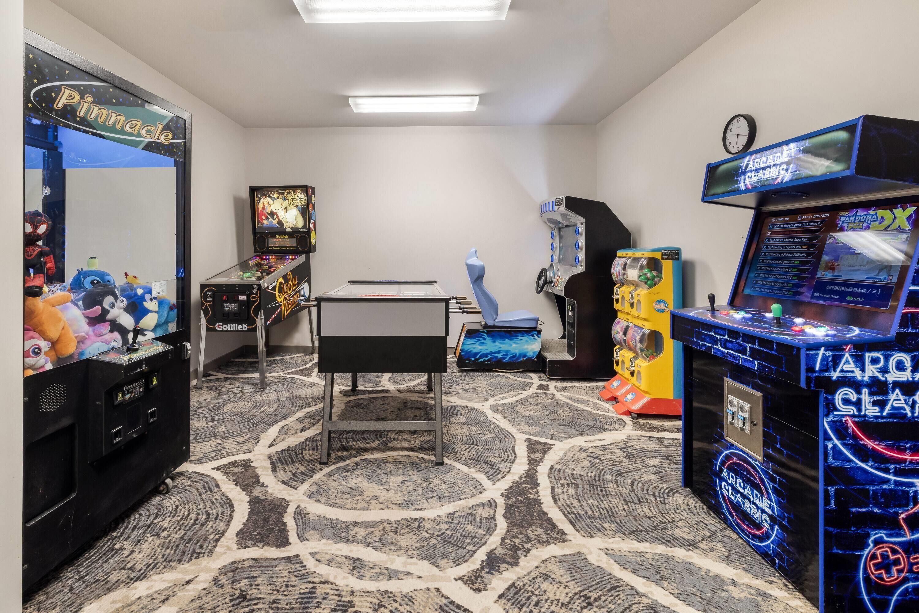 Una habitación con máquinas de videojuegos, mesa de ping pong y peluches en estantes.