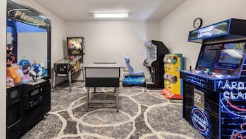 Una habitación con máquinas de videojuegos, mesa de ping pong y peluches en estantes.