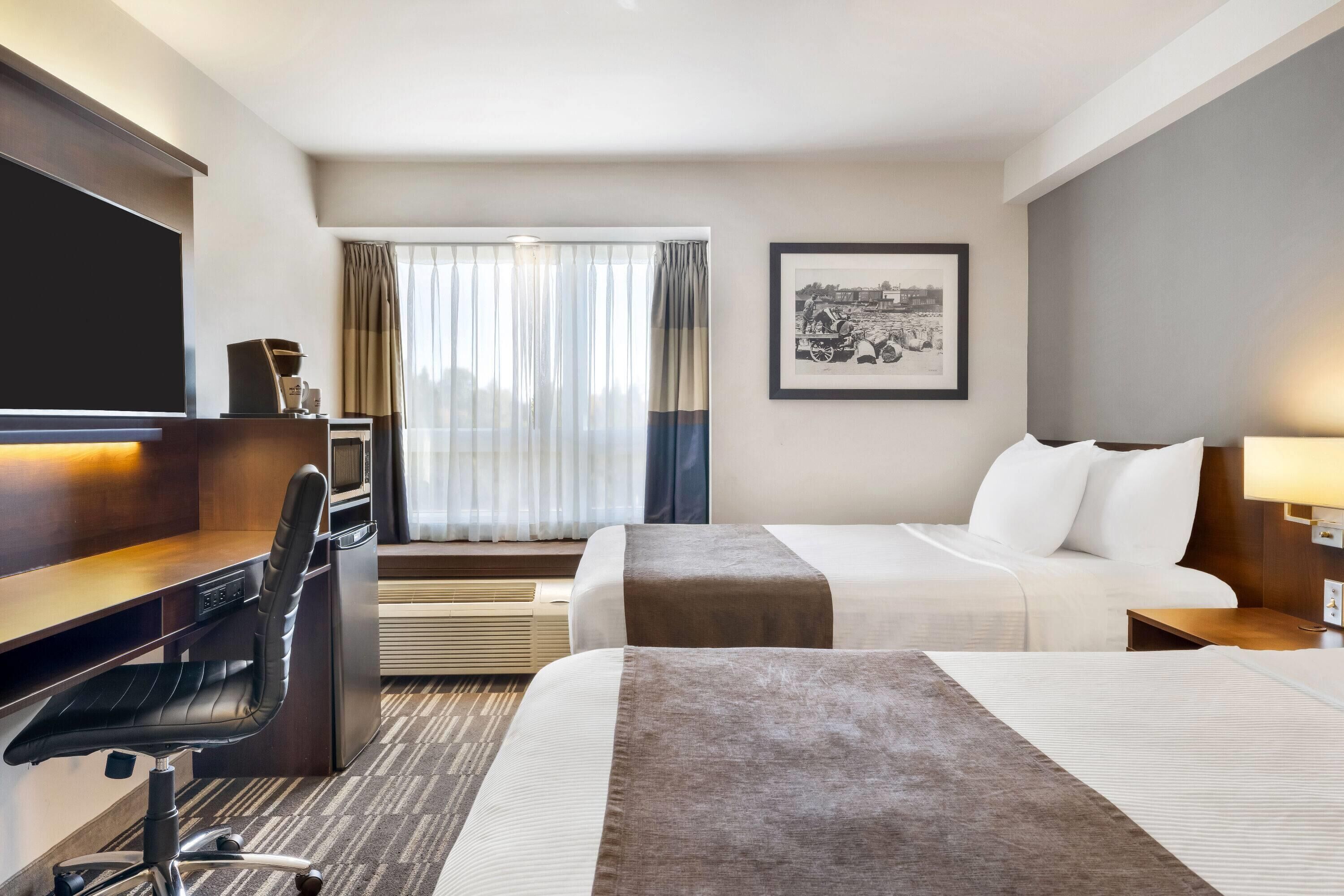 Een hotelkamer met een bed, een bureau met stoel, een televisie en een raam met gordijnen.