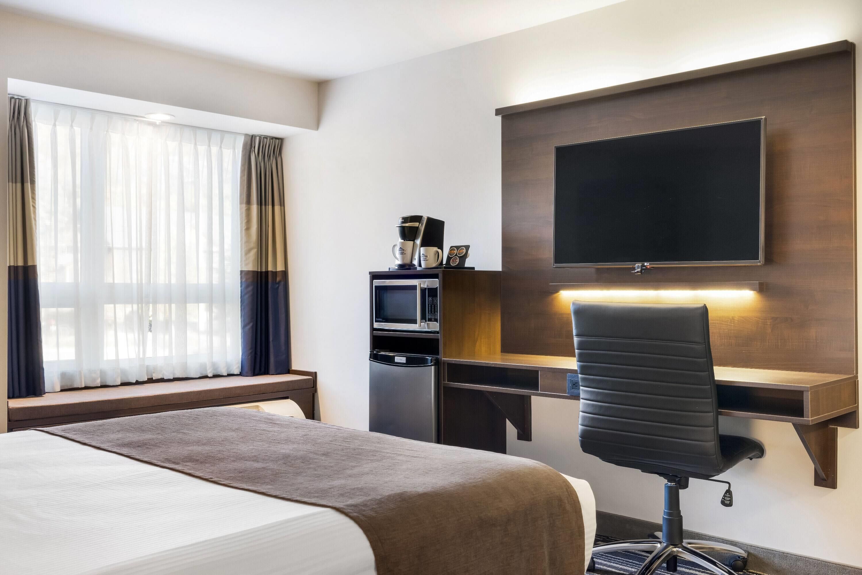 A hotel room with a bed, a desk with a computer, a TV, and a microwave.