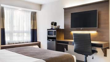 A hotel room with a bed, a desk with a computer, a TV, and a microwave.