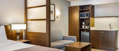 A hotel room with a bed, a sofa, a desk, a kitchenette, and a bathroom.