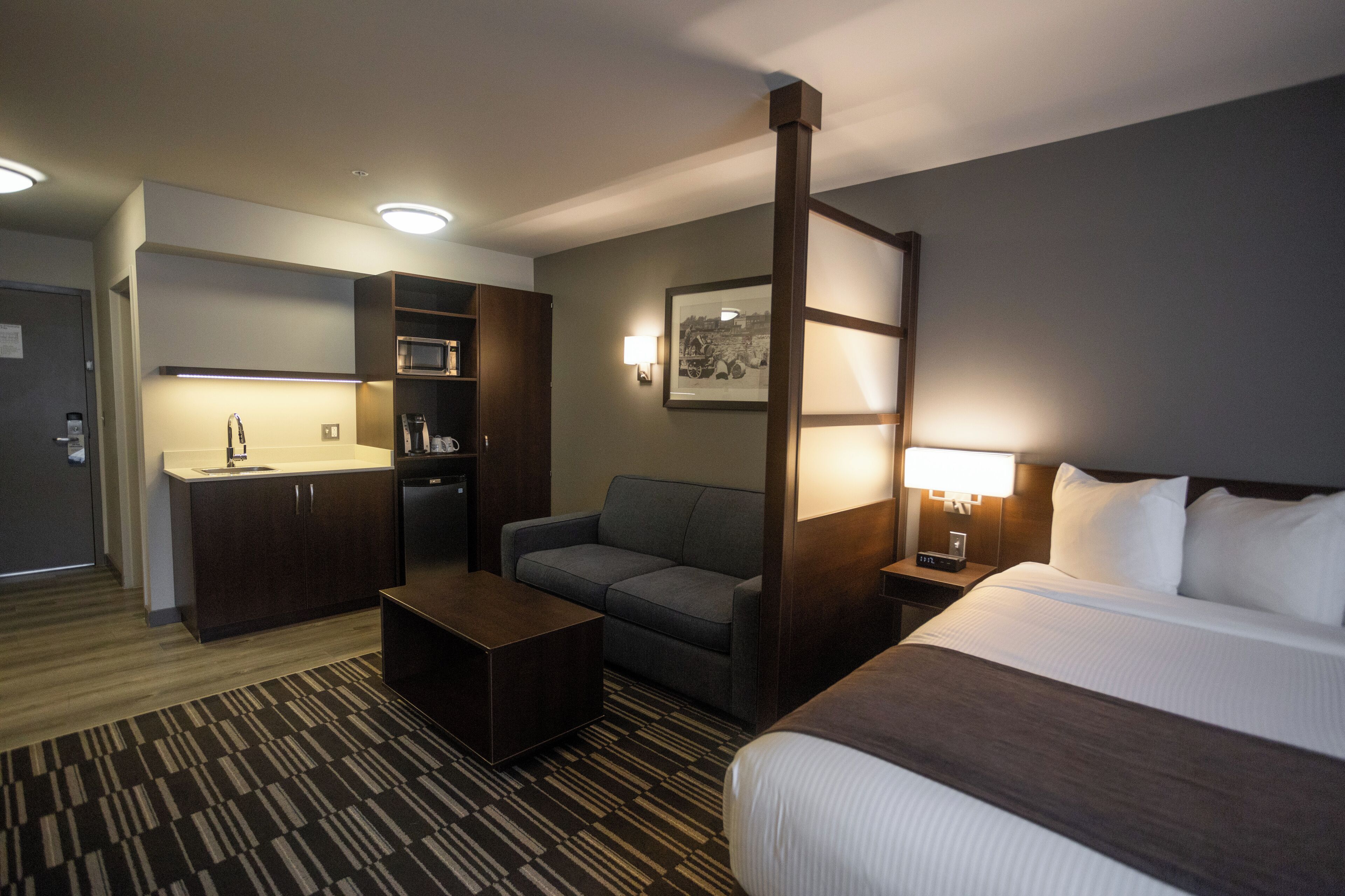 A hotel room with a bed, a sofa, a desk, a microwave, and a coffee machine.