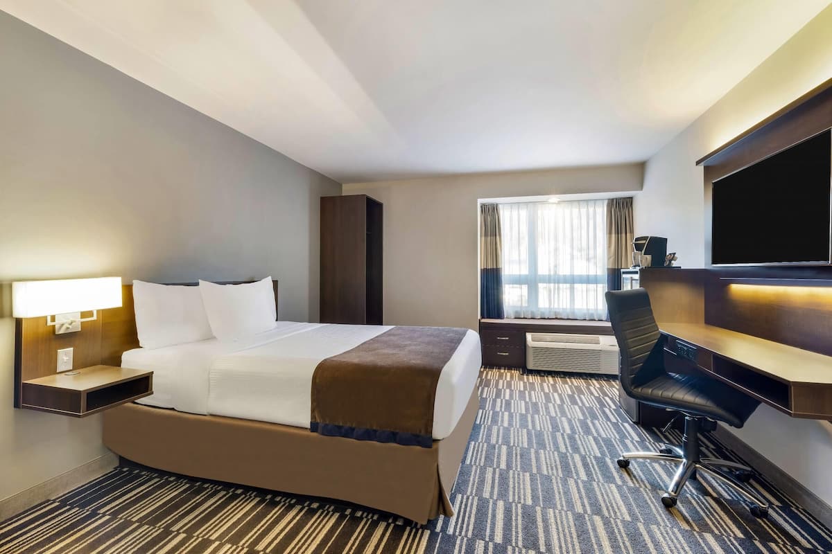 Une chambre d’hôtel avec un lit, un bureau, une chaise, une télévision et une fenêtre avec des rideaux.