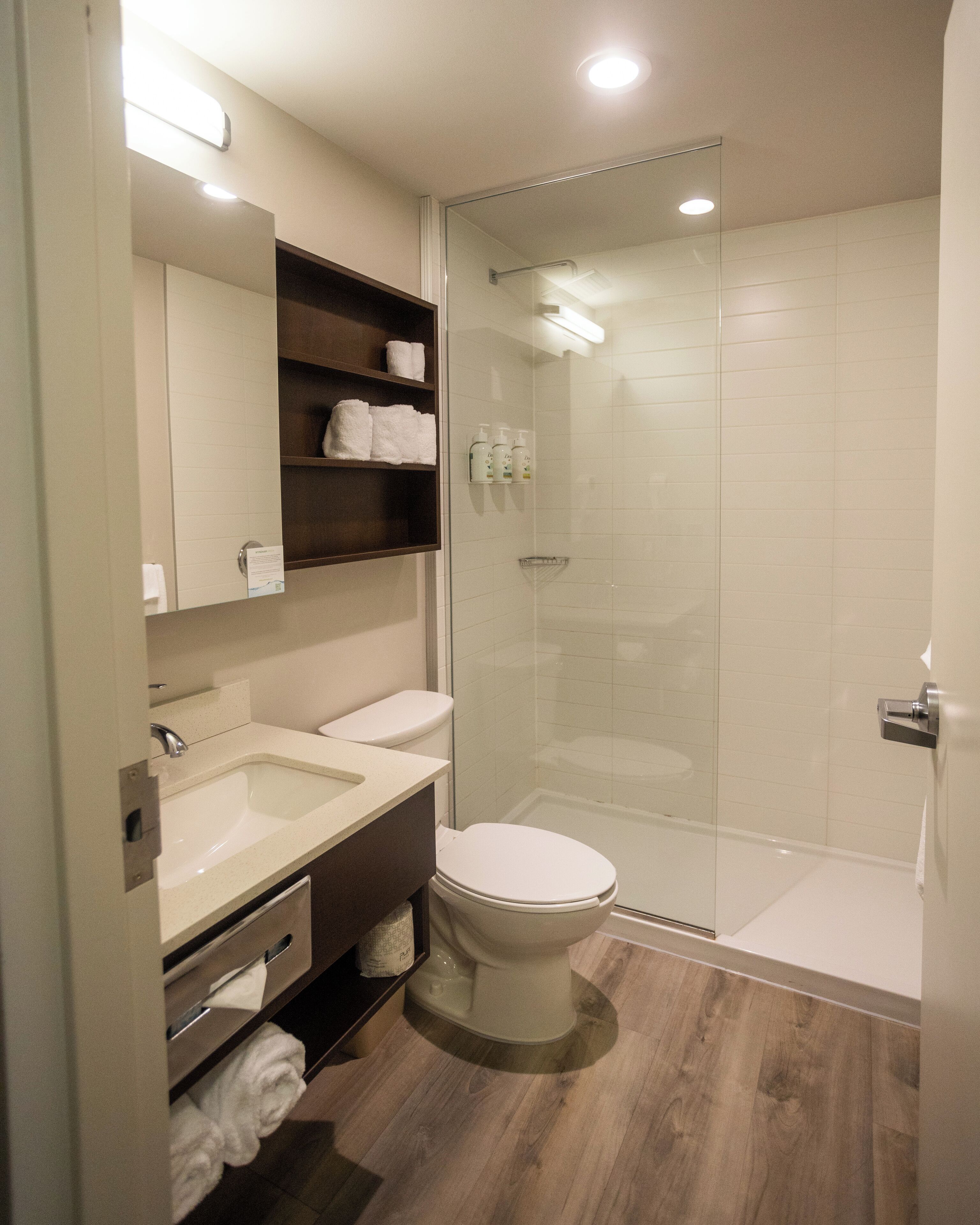 A modern bathroom with a glass-enclosed shower, a sink, a toilet, and a mirror with shelves holding towels.