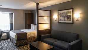 Une chambre d’hôtel comprenant un lit, un canapé, une table basse, un téléviseur fixé au mur et une fenêtre avec des rideaux.