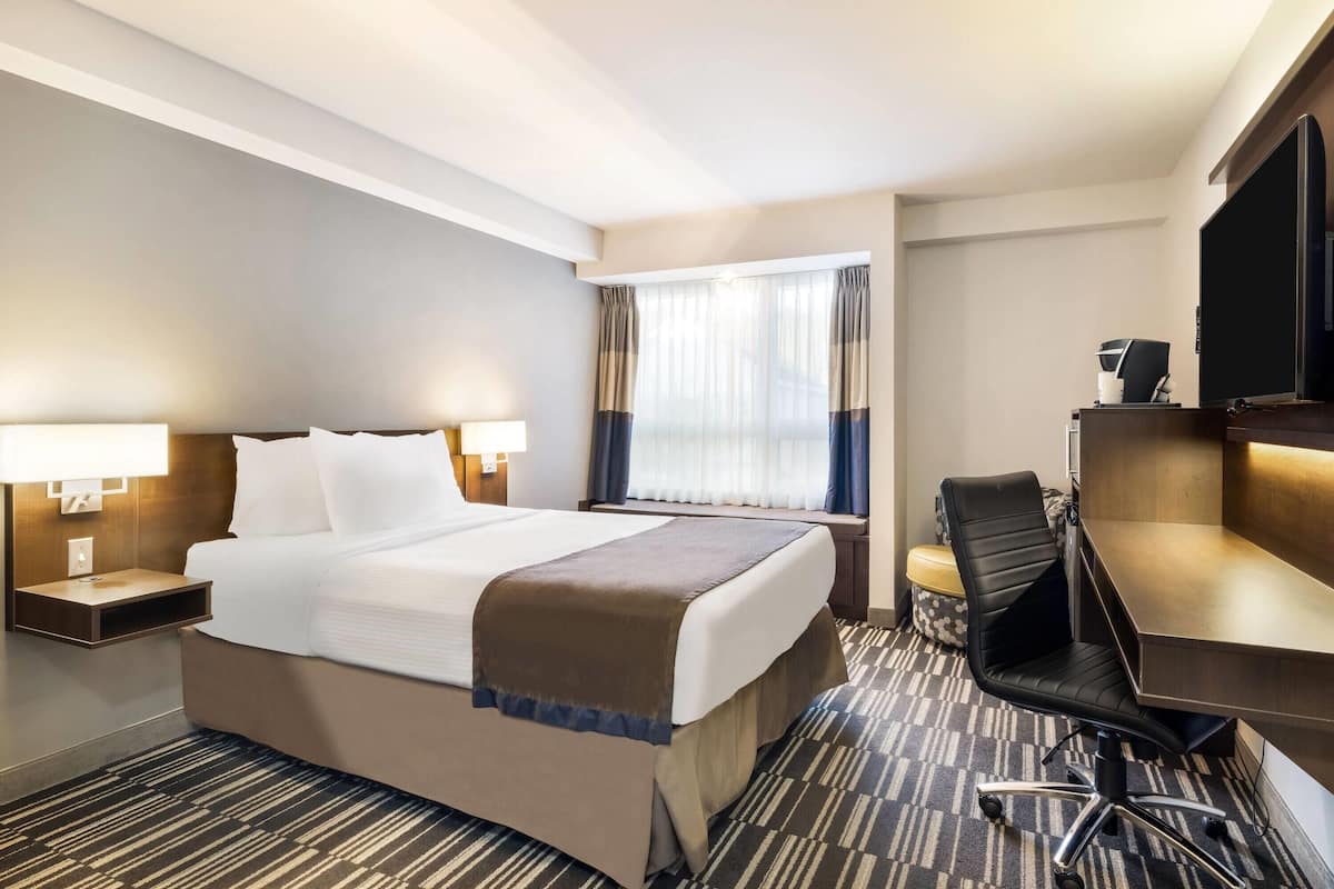 Une chambre d’hôtel avec un grand lit, des tables de chevet avec des lampes, un bureau avec une chaise et un téléviseur.