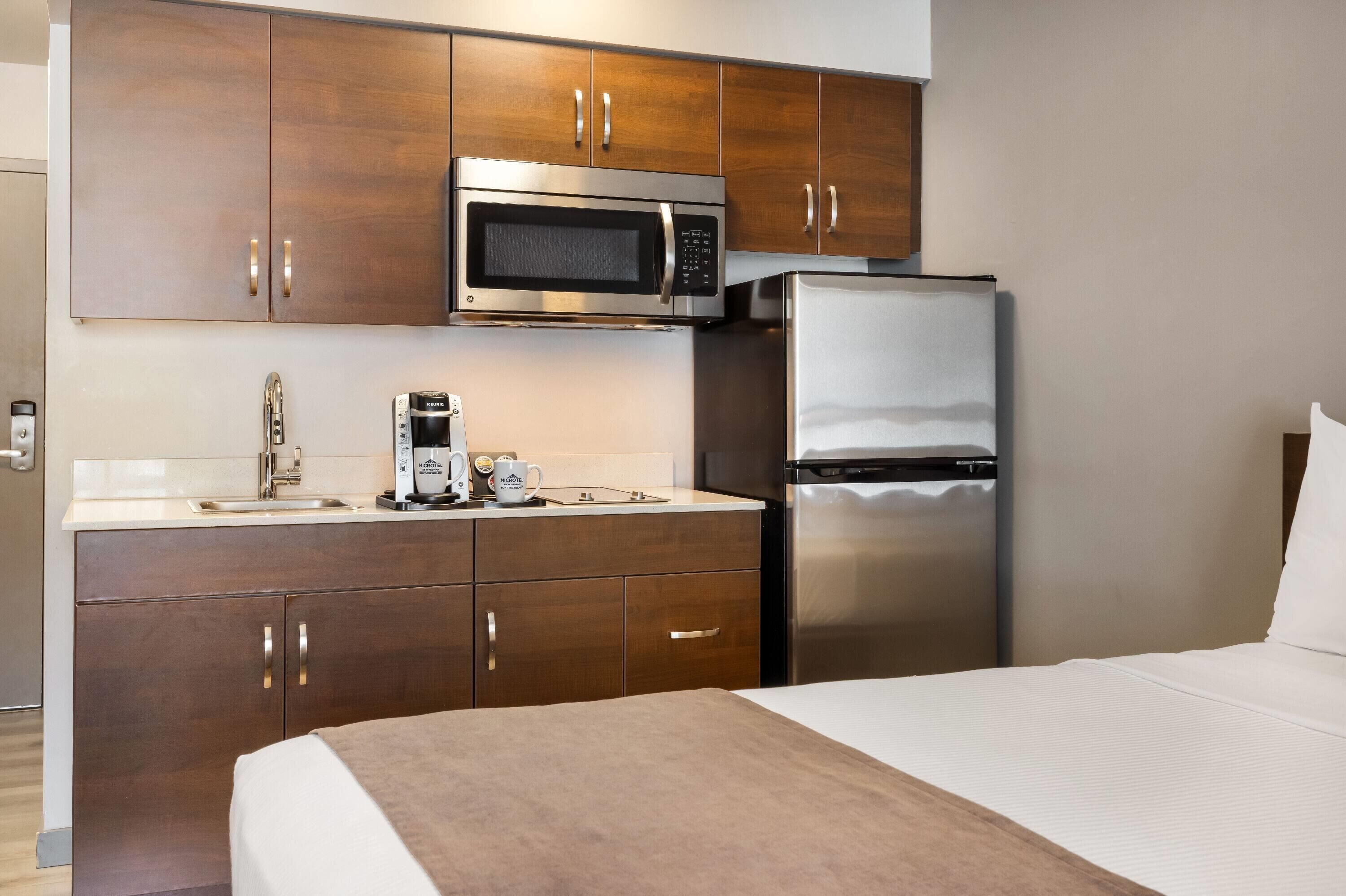 Una habitación de hotel compacta con kitchenette que incluye microondas, cafetera y refrigerador.