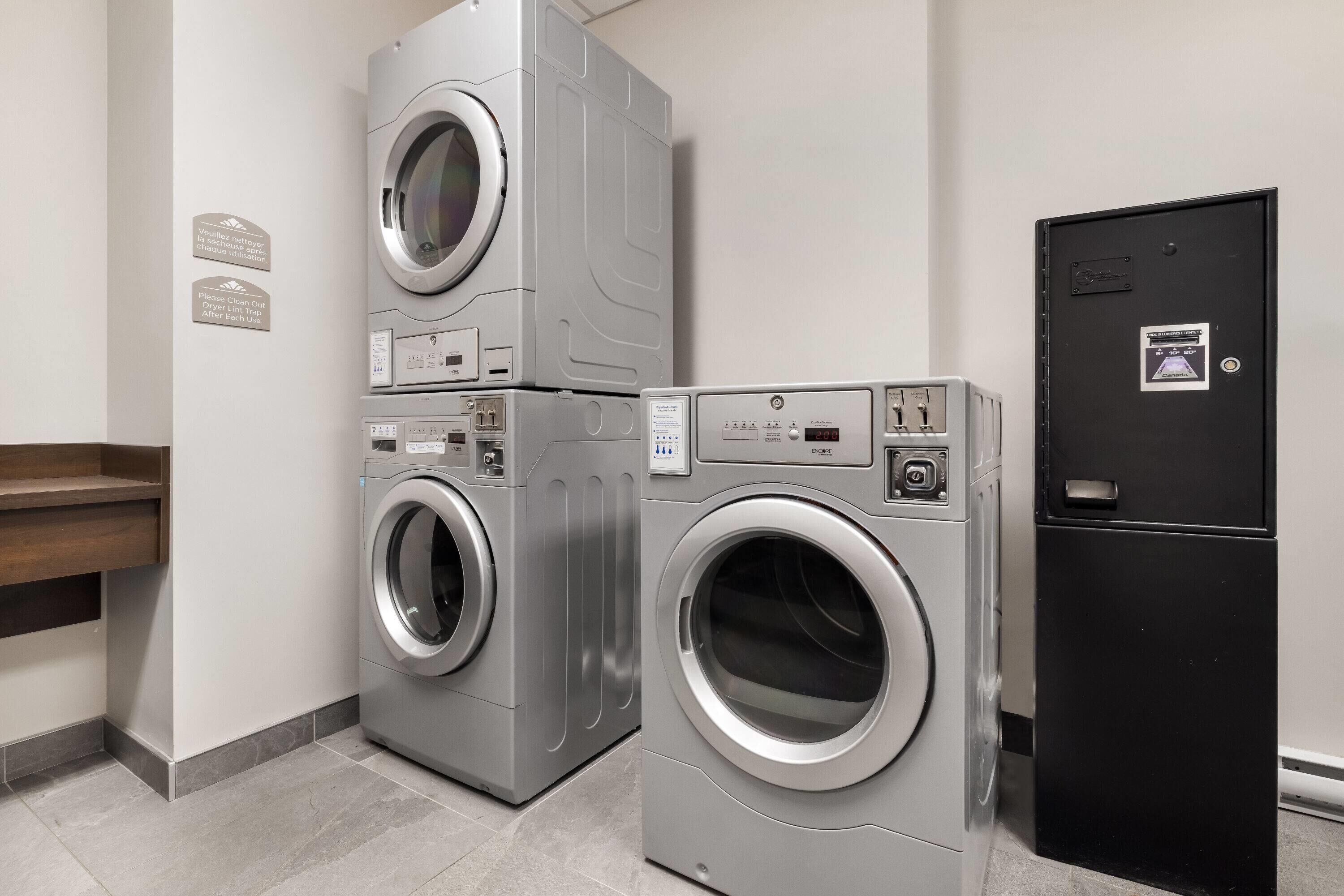 Een wasserette met gestapelde wasmachines en drogers, een zwarte deur naar de technische ruimte, en een bordje dat aan de muur hangt.