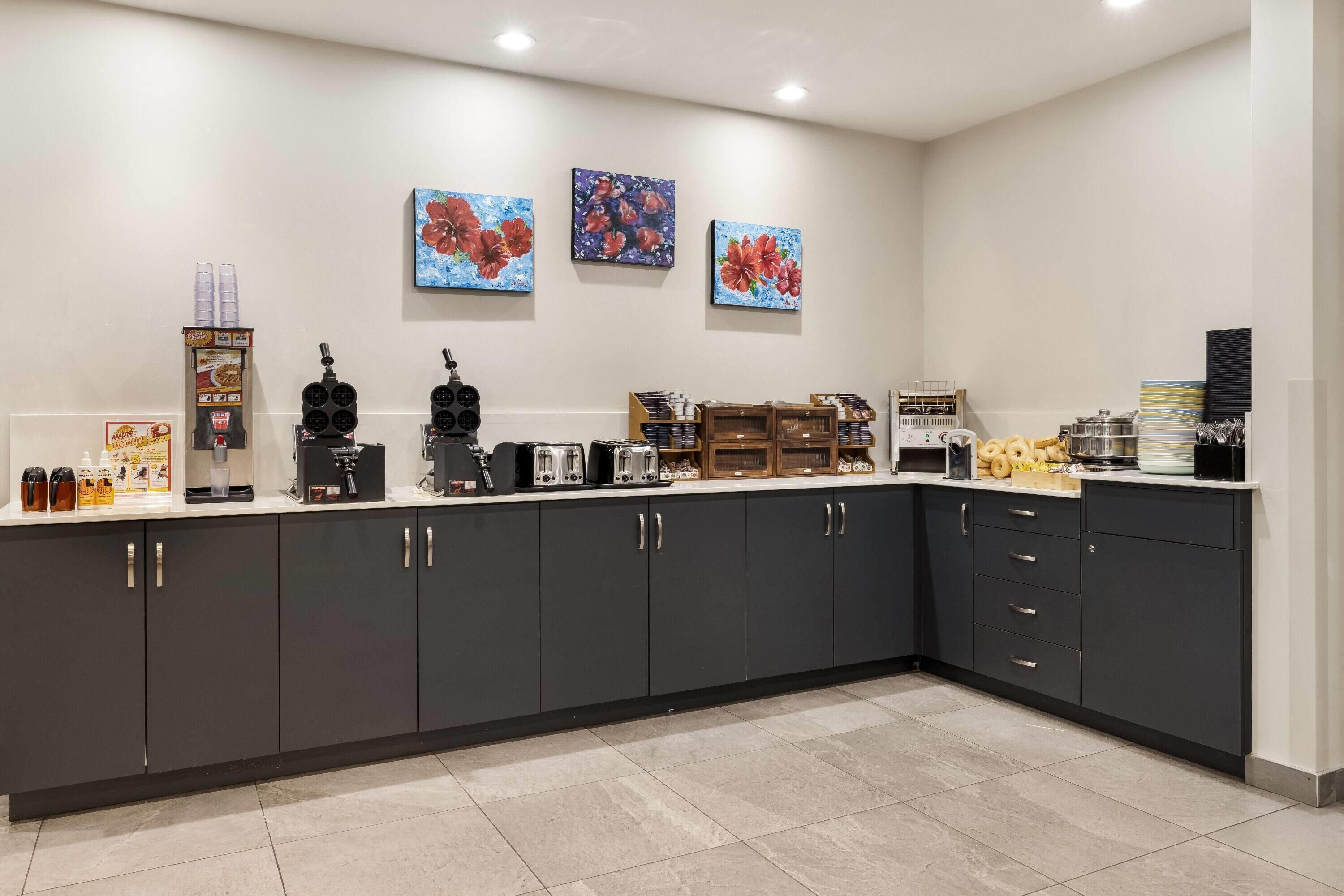 A modern kitchen with dark cabinets, a coffee station, and three floral paintings on the wall.