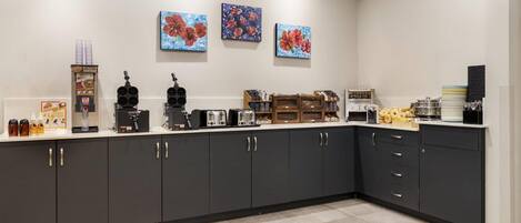 A modern kitchen with dark cabinets, a coffee station, and three floral paintings on the wall.