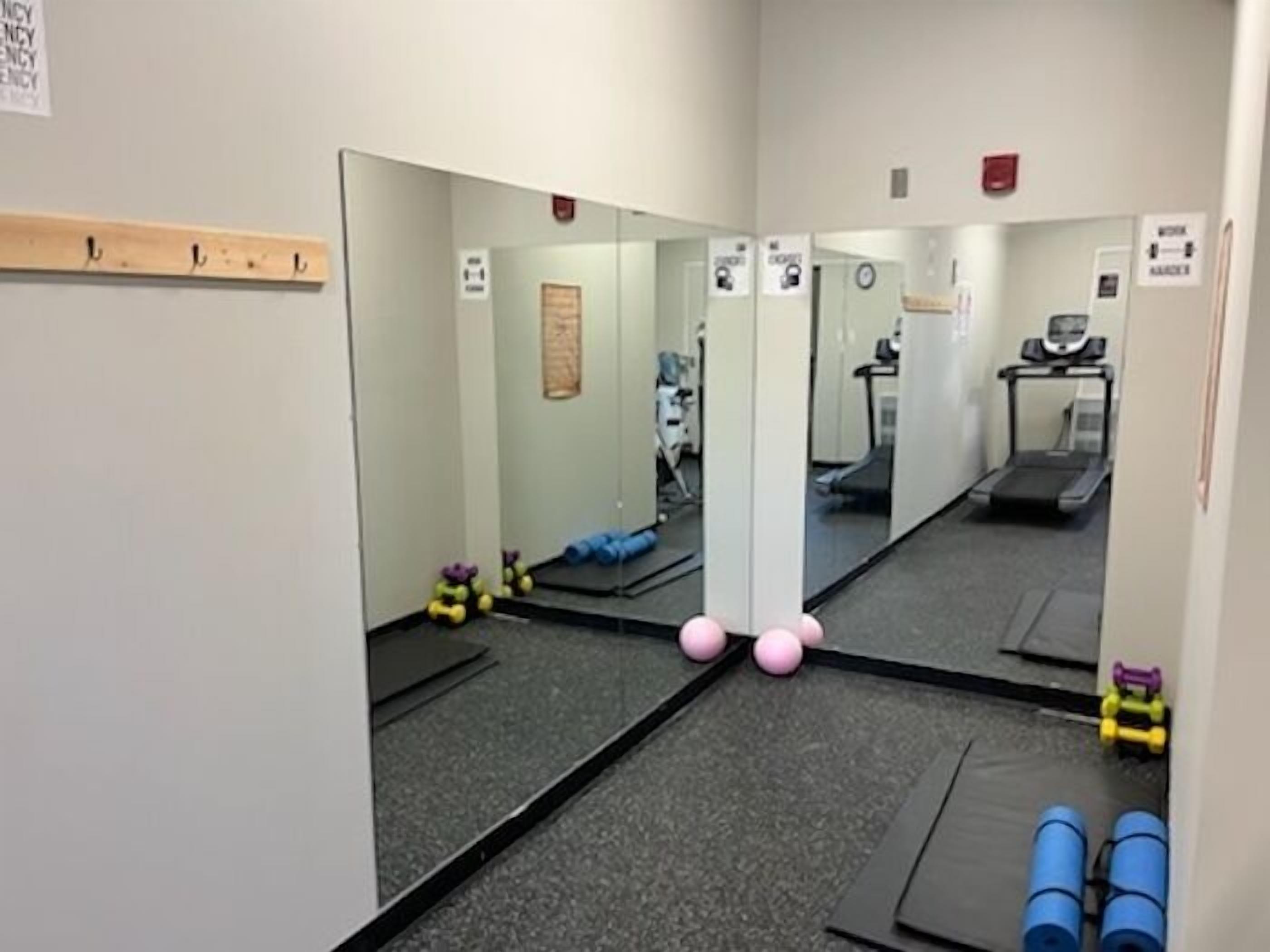 Une salle de sport équipée de machines d’exercice, de miroirs et d’un tapis de course.