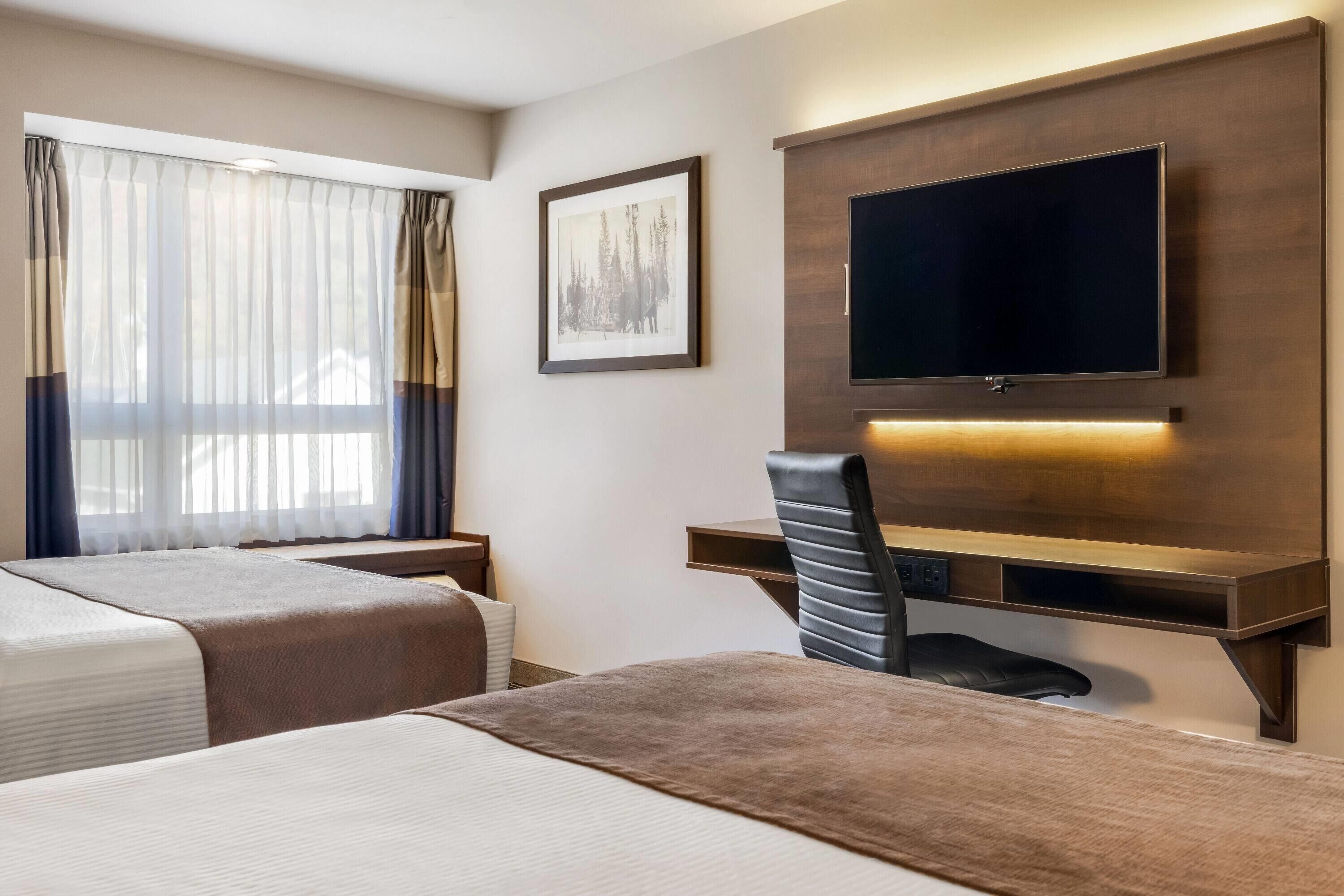 Een hotelkamer met twee bedden, een bureau, een stoel, een televisie en een lijst met een afbeelding aan de muur.