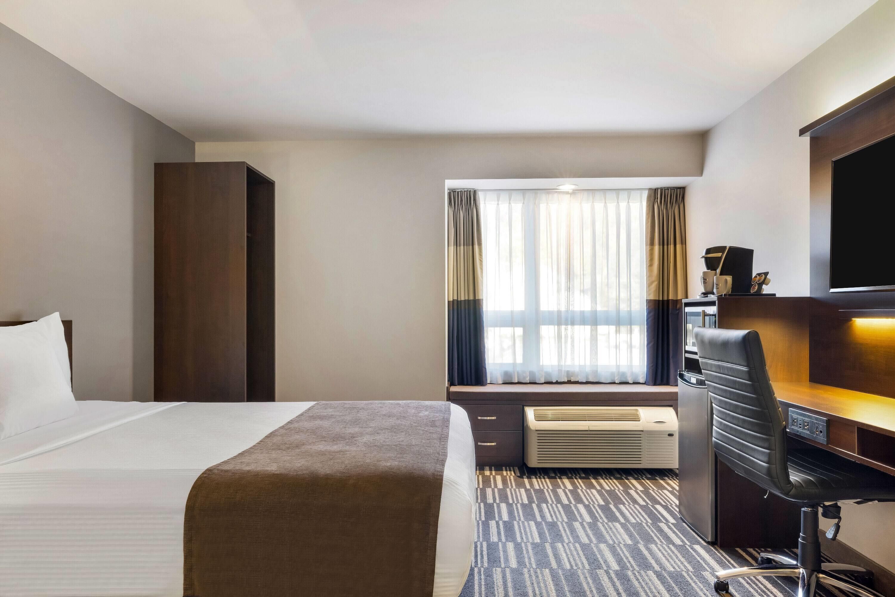 Una camera d'albergo con un letto, una scrivania con una sedia, una televisione e una finestra con tende.