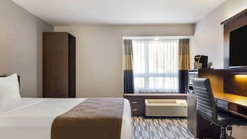 Una camera d'albergo con un letto, una scrivania con una sedia, una televisione e una finestra con tende.
