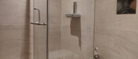 A modern bathroom with a glass-enclosed shower, a white toilet, and a small shelf.