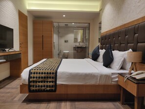 A modern hotel room with a large bed, a bedside table with a lamp, a TV, and a bathroom visible through an open door. - Meritas Countryside Resort - Lonavala (Mawal)
