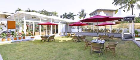 Un patio al aire libre con mesas, sillas, sombrillas rojas y plantas en macetas.