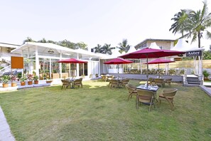 An outdoor patio area with tables and chairs, red umbrellas, and potted plants. - Meritas Countryside Resort - Lonavala (Mawal)