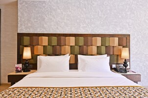 Habitación de hotel con un cabecero estampado, una cama bien hecha, dos lámparas de noche y una mesita de noche con un teléfono y un libro.