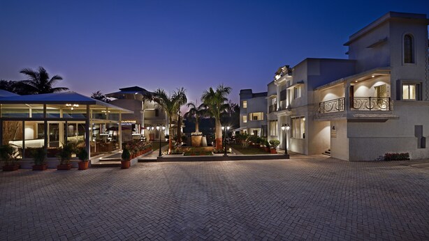 A courtyard with a fountain, palm trees, and a building with a balcony. - Meritas Countryside Resort - Lonavala (Mawal)