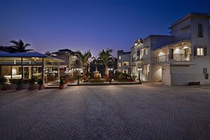 A courtyard with a fountain, palm trees, and a building with a balcony. - Meritas Countryside Resort - Lonavala (Mawal)
