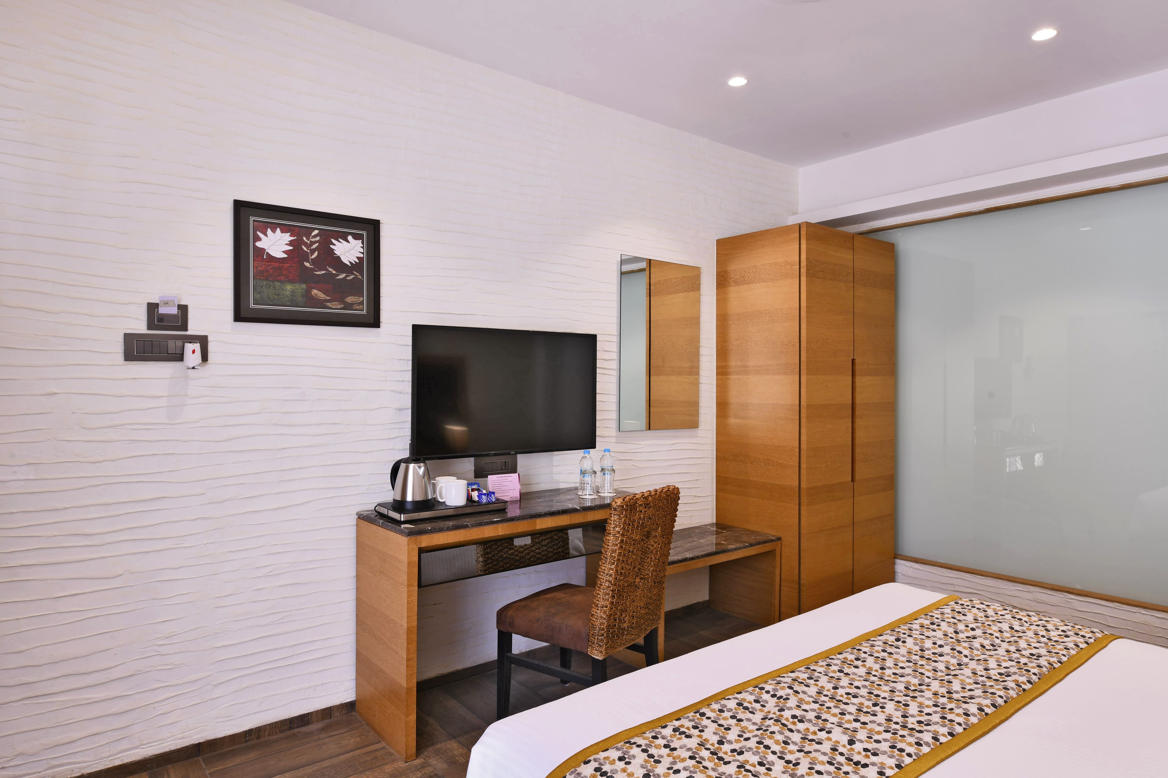 Una habitación de hotel moderna con un escritorio de madera, un televisor de pantalla plana, una cama grande y un armario.