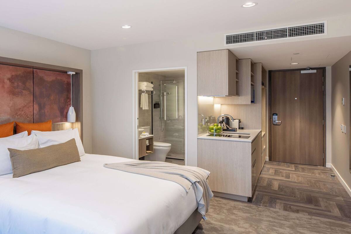 A modern hotel room with a large bed, a small kitchenette, and a separate bathroom.
