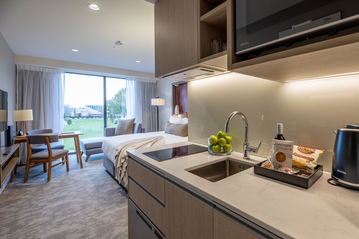 Una habitación de hotel moderna con kitchenette, una cama, un escritorio y vistas al exterior.