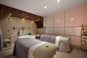 A modern spa room with a large bathtub, two treatment beds, a wooden ceiling, and a wall-mounted shelf with towels. - Sudima Christchurch City (Christchurch)