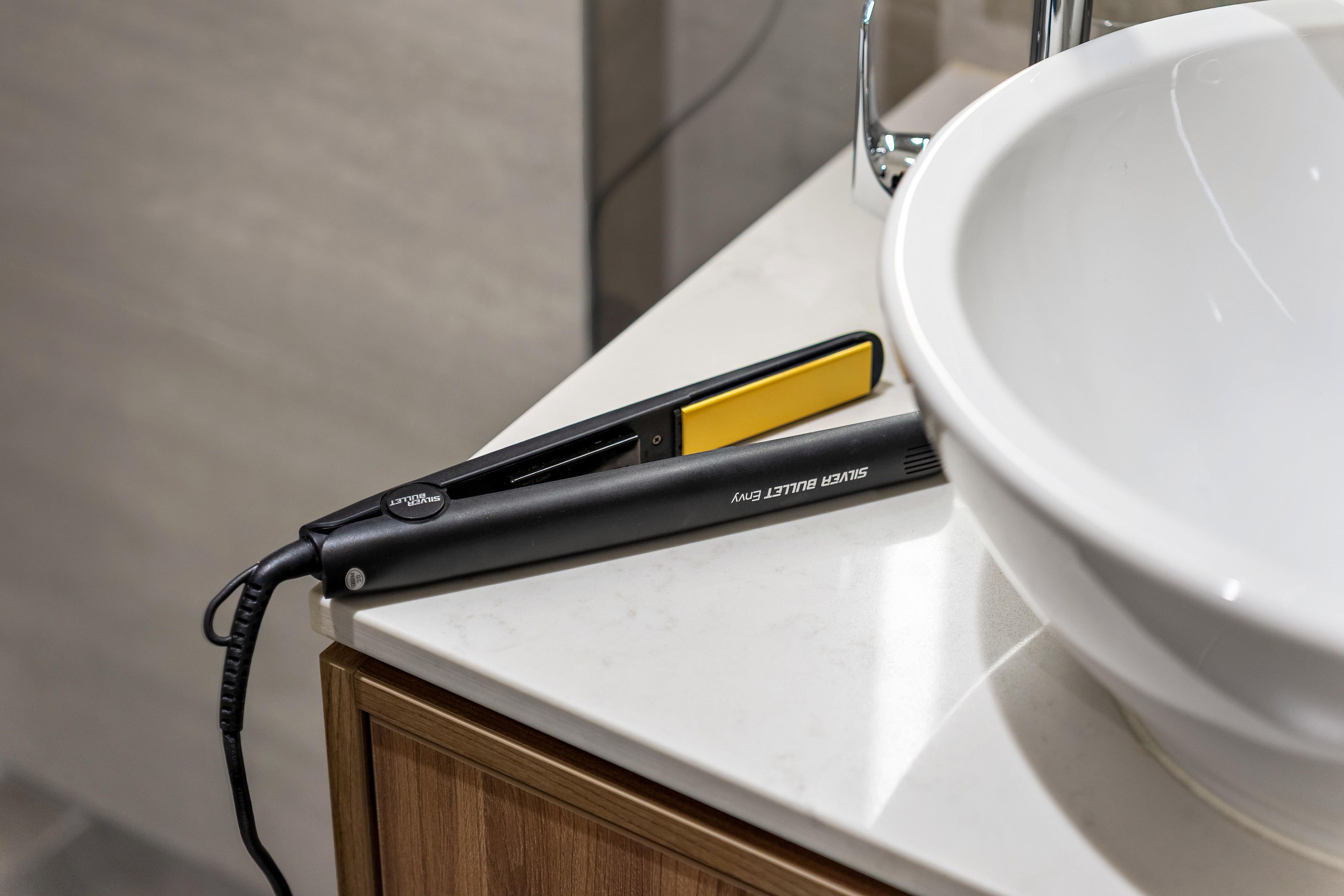 A bathroom with a white sink, a wooden cabinet, and a black and yellow hair straightener on the countertop.