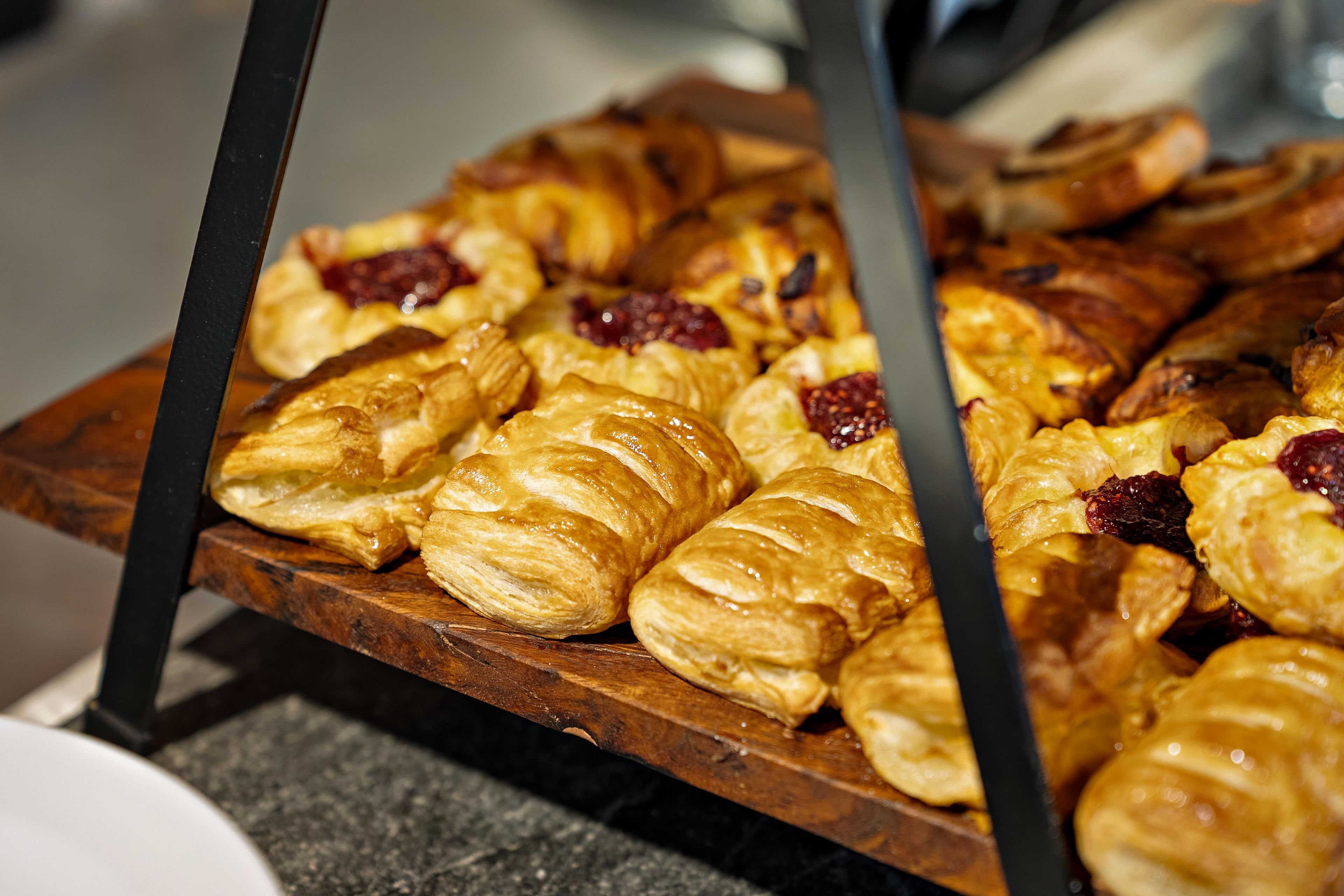Une planche en bois garnie de viennoiseries, notamment des croissants et des pâtisseries aux fruits.