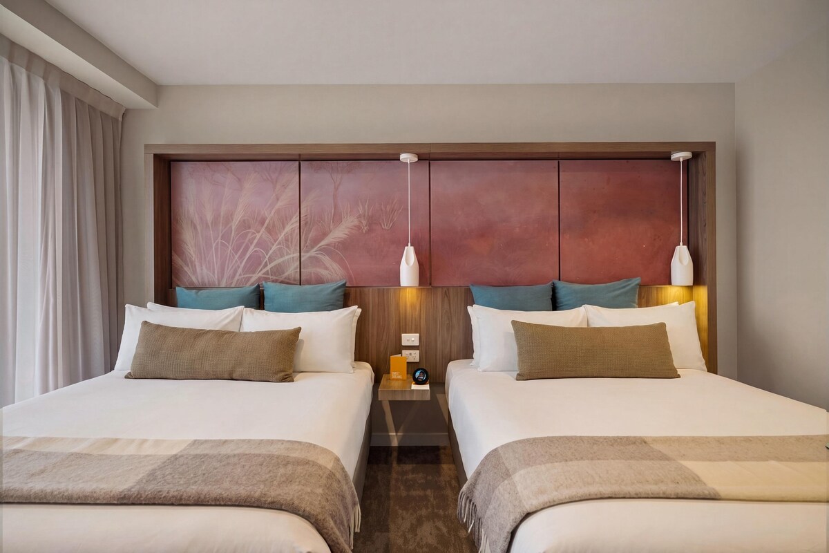 A hotel room with two beds, a wooden headboard, and a nightstand with a clock and a small table.