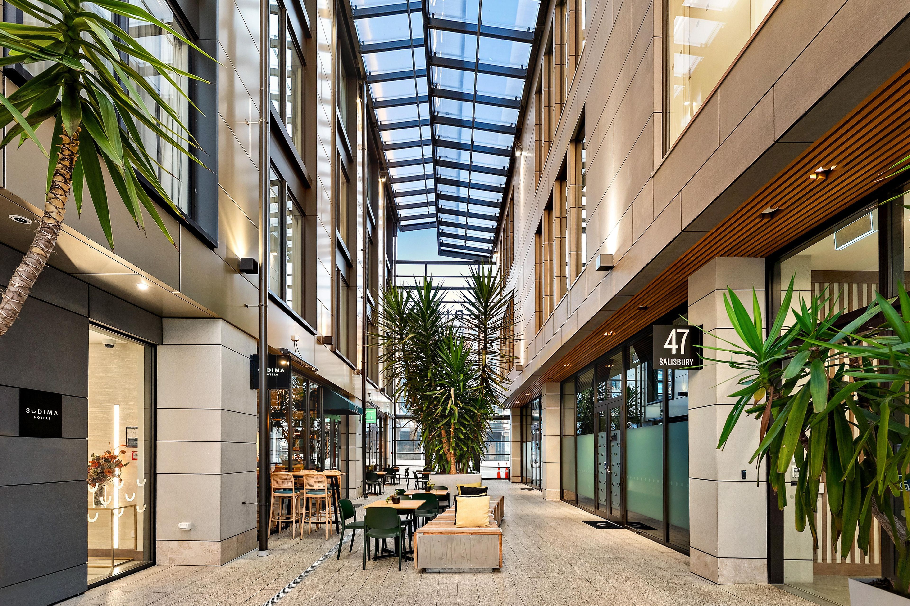 A modern atrium with a glass ceiling, indoor seating, and a hotel sign.