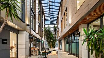 A modern atrium with a glass ceiling, indoor seating, and a hotel sign.