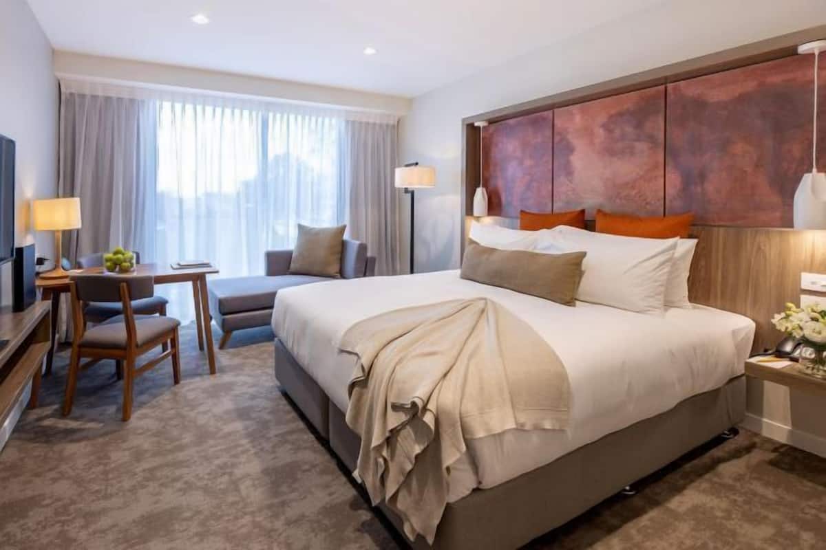A hotel room with a large bed, a desk, a chair, and a TV.
