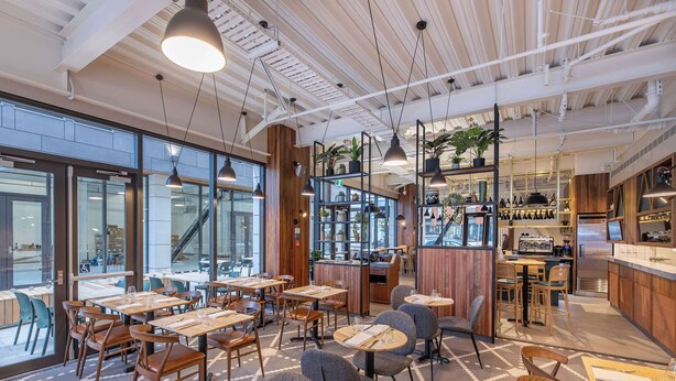A modern restaurant with wooden tables and chairs, large windows, and hanging pendant lights. - Sudima Christchurch City (Christchurch)